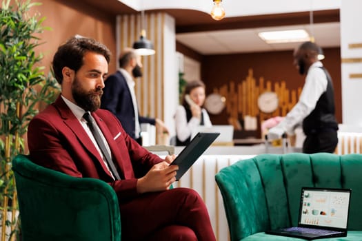 Employee looks over meeting notes waiting to do check in before attending important international conference. Young businessman at hotel travelling for work, reading documents in lobby.