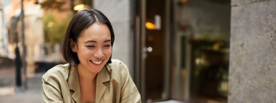 Smiling young woman working from cafe or co-working space, sitting with laptop, studying or doing homework, looking happy.