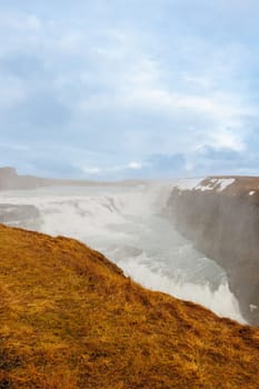 Gullfoss cascade in Iceland, consists of majestic river stream and untouched arctic nature. Nordic scenic route with huge waterfall and stream flowing alongside snow covered hills.