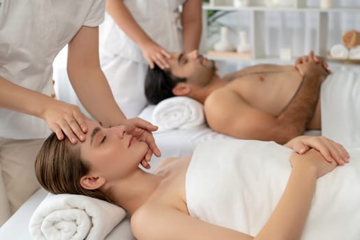 Caucasian couple enjoying relaxing anti-stress head massage and pampering facial beauty skin recreation leisure in dayspa modern light ambient at luxury resort or hotel spa salon. Quiescent