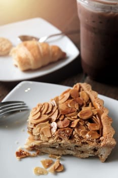 Eating almond pie in the cafe, closeup piece of almond pie on white plate. 