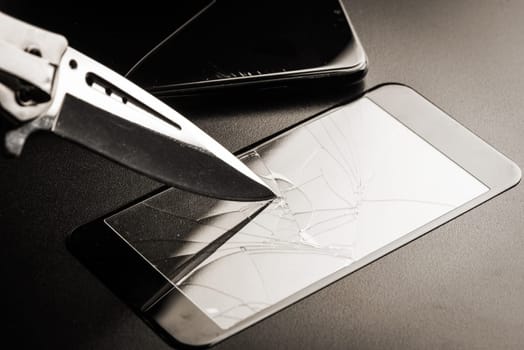 closeup broken tempered glass screen protector for smartphone. Testing the hardeness with knife.