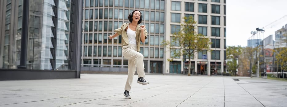 Happy people in city. Upbeat young girl dancing on street in headphones, listening music in headphones.