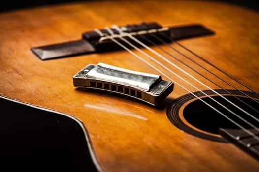 vintage wooden harmonica lying on an old acoustic guitar.