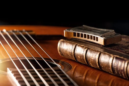 vintage wooden harmonica lying on an old acoustic guitar.