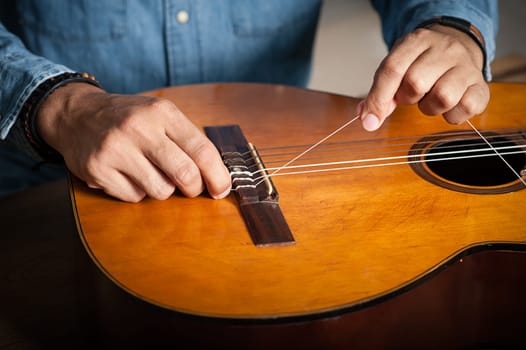 closeup man's hand changing strings on his old acoustic guitar.
