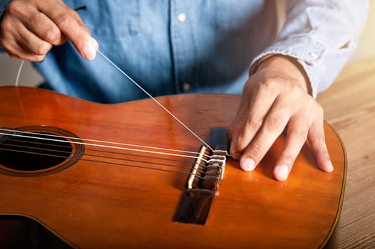 closeup man's hand changing strings on his old acoustic guitar.