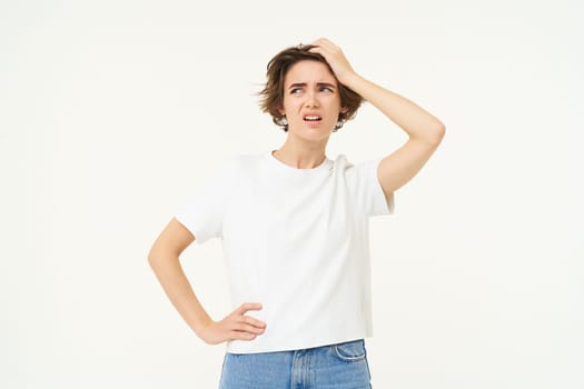 Portrait of woman looking troubled, slap her forehead, standing thoughtful and frowning, facing complicated problem, standing over white studio background.