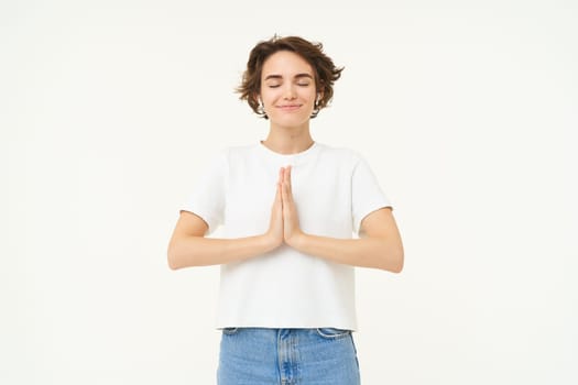 Portrait of brunette young woman holds hands together, namaste gesture, say thank you, grateful, express gratitude and joy, stands over white background. copy space