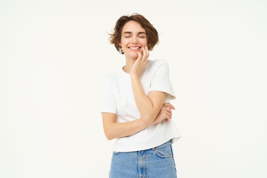 People and lifestyle. Portrait of smiling, gentle young brunette woman, gazing at camera, looking at something lovely, standing over white studio background.