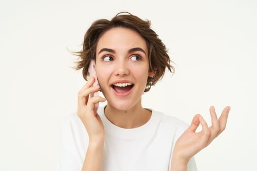 Portrait of happy, chatty young woman talking on mobile phone, using smartphone, calling someone, standing over white studio background.