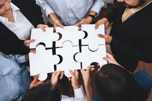 Diverse corporate officer workers collaborate in office, connecting puzzle pieces to represent partnership and teamwork. Unity and synergy in business concept by merging jigsaw puzzle. Concord