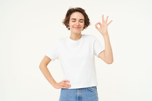 No problem. Portrait of young woman standing in confident pose, shows okay, ok, zero gesture, stands over white studio background.