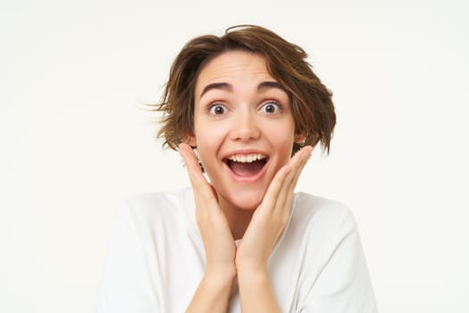 Portrait of girl with surprised face, makes shocked expression, stands over white background. Emotions and people concept