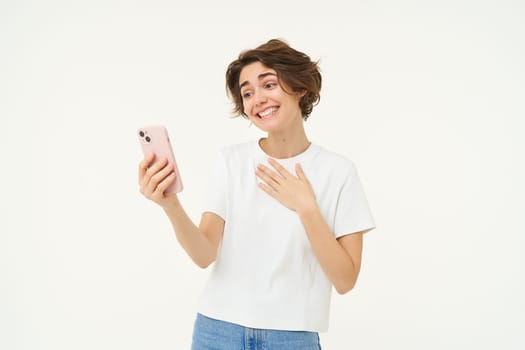 Portrait of girl talking on mobile phone, video chats with friends on smartphone, standing over white studio background.