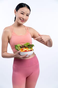 Young sporty Asian woman in sportswear holding salad bowl fill with vibrant of fruit and vegetable. Natural youthful and fit body lifestyle with balance nutrition on isolated background. Vigorous