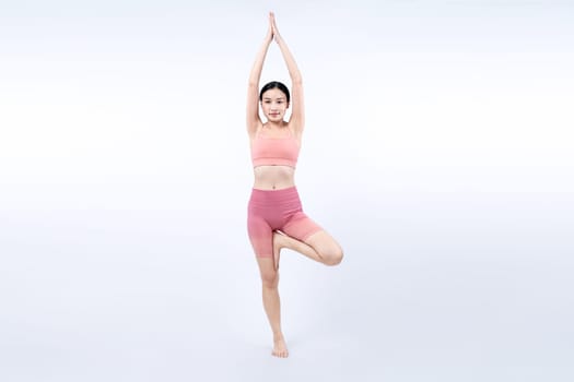 Asian woman in sportswear doing yoga exercise in standing pose on fitness as her workout training routine. Healthy body care and meditation yoga lifestyle in full shot on isolated background. Vigorous