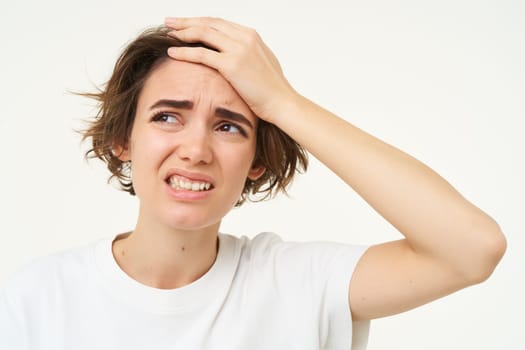 Portrait of young upset woman, slaps her forehead, facepalm, touches head and looks like she is in pain, has headache or migraine, isolated over white background.