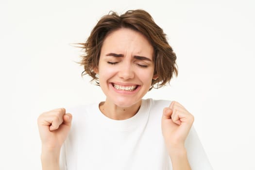 Image of happy, excited brunette woman, clenches her fists, dancing in excitement, feeling amused, standing over white background.