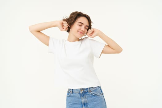 Portrait of smiling, pleased woman stretching hands, waking up after sleep, standing over white background. Copy space