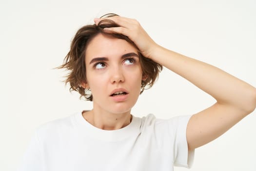 Bothered and annoyed woman, holds hand on head and sighing, rolling her eyes from irritation, upset by something, standing over white background.