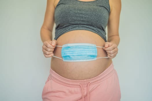 Belly of a pregnant woman holding medical mask close up.