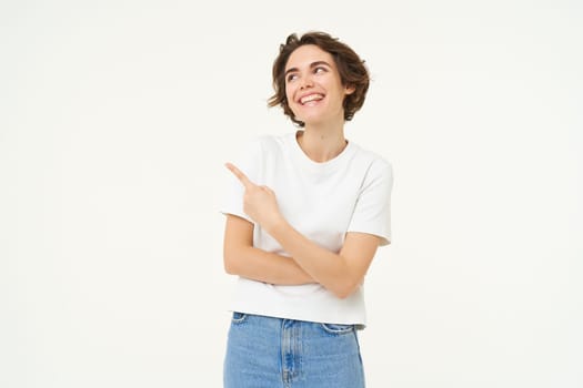 Portrait of brunette girl showing banner, pointing finger left, advertising, standing over white background.