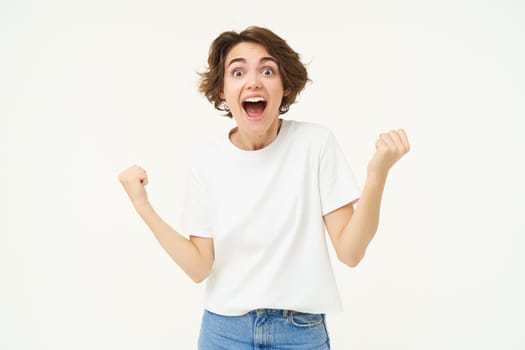 Portrait of happy, excited young woman winning, triumphing, feeling like champion, posing over white background.