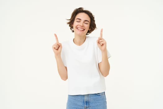 Image of carefree girl, laughing and smiling, pointing fingers up, showing promo offer, banner on top, posing over white studio background. Copy space