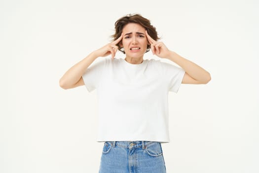 Image of distressed, upset young woman touches her head, has headache, suffers from migraine, stands over white background. Copy space