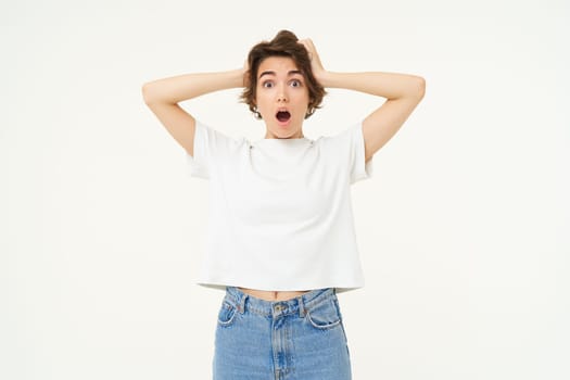 Image of woman with shocked face, looks frightened in panic, stands against white studio background. Copy space