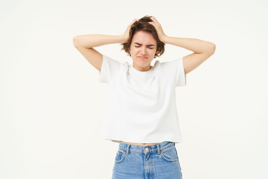 Portrait of woman in panic, grabs her head, feeling troubled, has big problem, stands anxious against white backgrond.