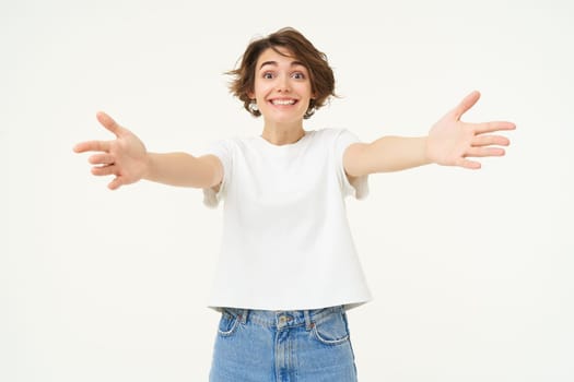 Portrait of beautiful, friendly woman stretching hands, hugging, extending arms for cuddle, embracing someone, standing against white background.