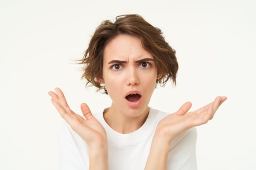 Close up of shocked brunette woman, shrugging and looking disappointed, posing over white studio background.