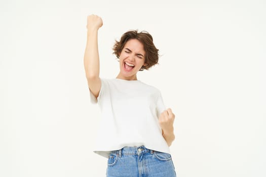 Portrait of happy, excited young woman winning, triumphing, feeling like champion, posing over white background.