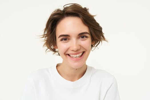 Close up portrait of brunette girl with short haircut, smiling and looking happy, posing over white background.