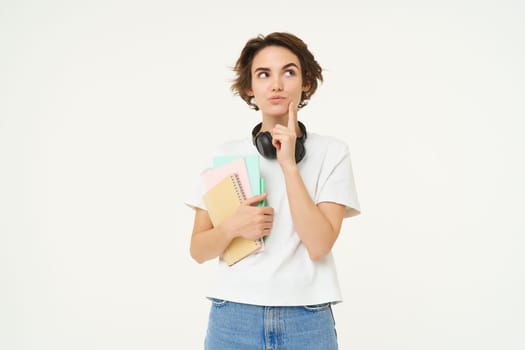 Portrait of brunette woman thinking, student with notebooks, looking thoughtful, making decision, standing over white studio background.