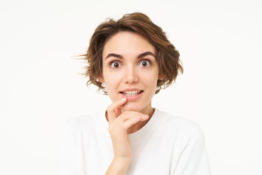 Close up portrait of woman looking with interest, listening, staring with curiosity, gasping at camera, standing over white background. Copy space