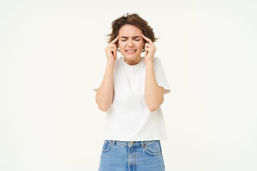 Image of distressed, upset young woman touches her head, has headache, suffers from migraine, stands over white background. Copy space