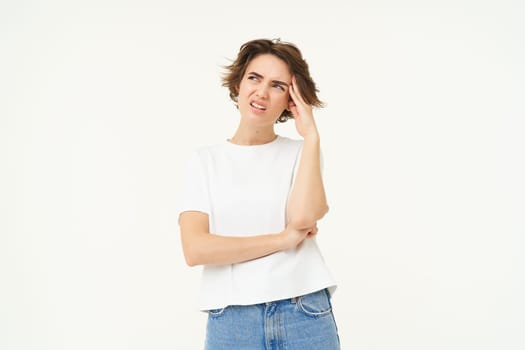 Portrait of woman looking troubled, thinking and frowning, having complicated situation, standing over white studio background.