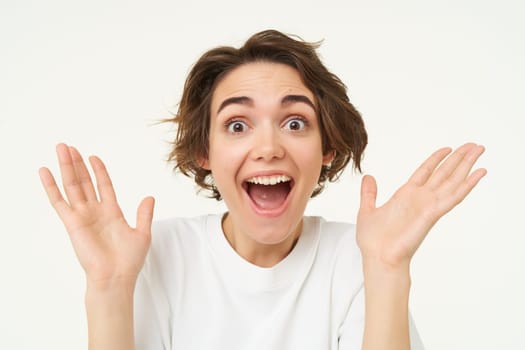 Close up portrait of excited brunette woman, gasping and smiling, claps hands and looks amazed, stands over white background.