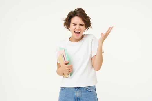 Stressed young girl student, woman screams, stands with notebooks and folders, looks depressed, stands over white background.