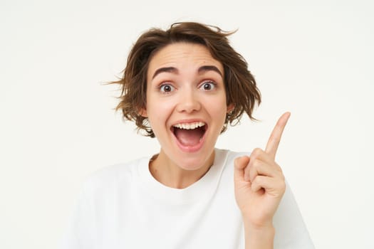 Close up of excited smiling woman, pointing finger up, showing number one, has an idea, thinking of a plan or solution, standing over white background.