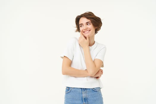 Portrait of young woman in casual clothes, laughing and smiling, touching her face without blemishes, standing over white background. Copy space