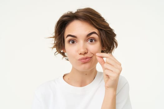 Close up portrait of brunette woman zip her lips, shows gesture to keep mouth shut, makes promise to safe someones secret, stands over white background.
