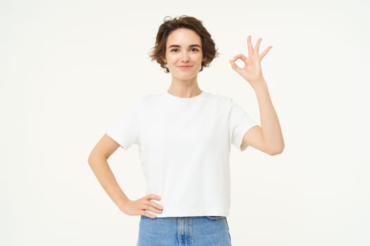 No problem. Portrait of young woman standing in confident pose, shows okay, ok, zero gesture, stands over white studio background.