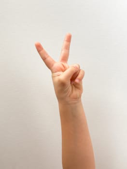 Peace gesture with childs hand on simple white background.