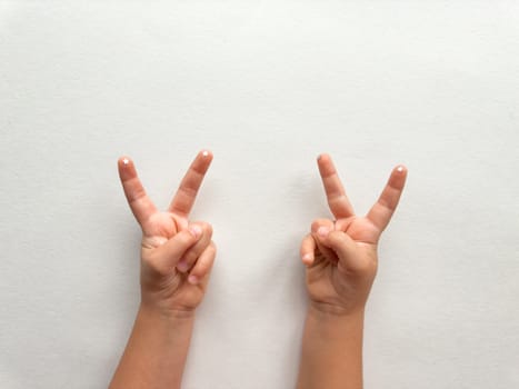 Childs hands showing peace sign on minimalist white background.