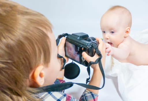 a baby with a hemangioma on his neck lies on a white background. baby photography. an older brother with a camera shoots a little sister