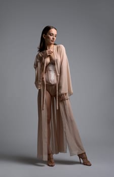 Slim girl in romantic underwear and long dressing-gown full-length shot against gray wall